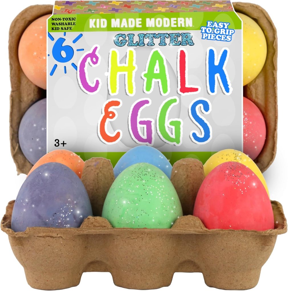 A carton of six colorful, glittery chalk eggs in a variety of pastel colors, including purple, blue, green, orange, red, and yellow, labeled as 'Kid Made Modern Glitter Chalk Eggs' with a suggested age of 3+.